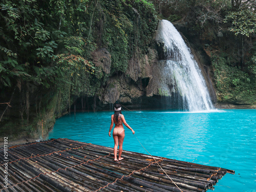 Fit woman alone on the bamboo raft in front of the waterfall with turquoise water in Kawasan Falls in Cebu Island, Philippines © Alohadunya