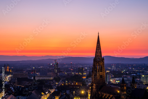 Germany, Intensive red sky sunset over muenster church steeple and skyline of city freiburg im breisgau in summer surrounded by black forest