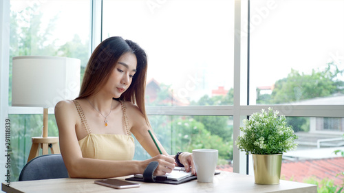 Young beautiful Asian woman enjoying a relaxing moment working and using mobile phone as mobile smart payment to pay for a coffee in the coffeeshop on a bright sunny day
