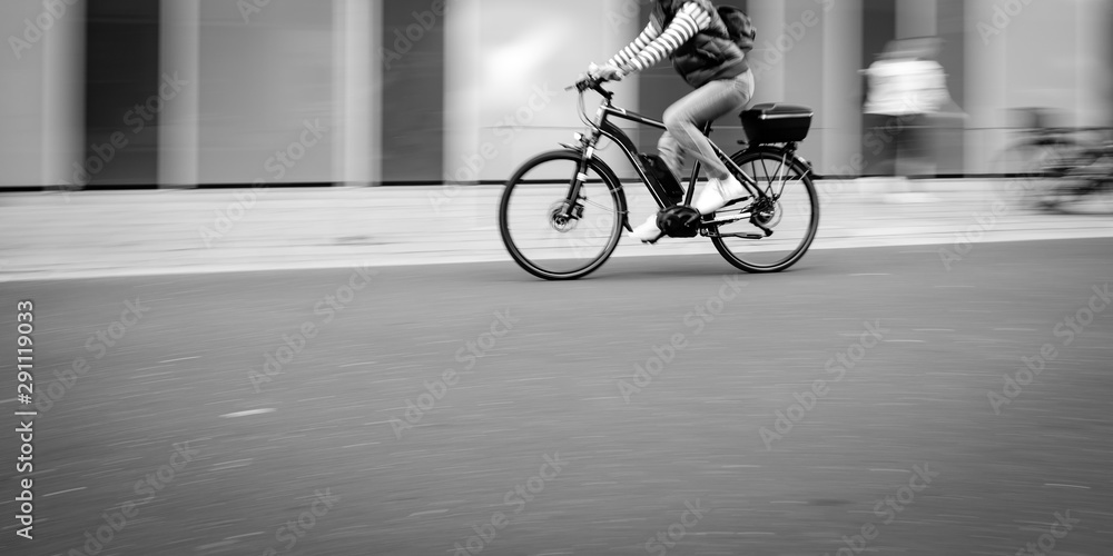 Frau fährt mit einem Pedelec auf einer Straße, Bewegungsunschärfe, monochrom Frau fährt mit einem Pedelec auf einer Straße, Bewegungsunschärfe, monochrom