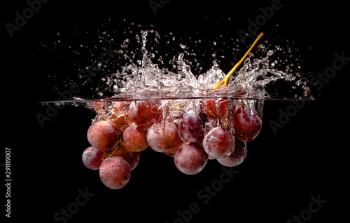 Isolated Red grapes splashing and sinking in water on black background with air bubbles.
