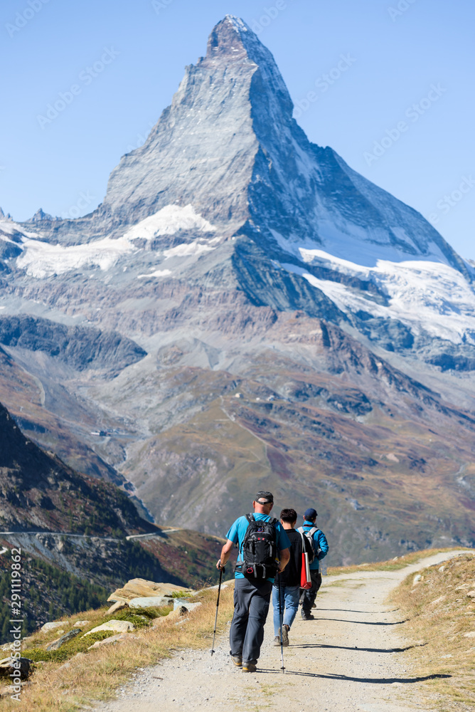 Group of tourists hiking in front of the mountain Matterhorn in Zermatt, Valais, Switzerland, beautiful blue sky, vertical
