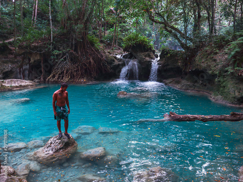 Fit man alone on the bamboo raft in front of the waterfall with turquoise water in Kawasan Falls in Cebu Island, Philippines