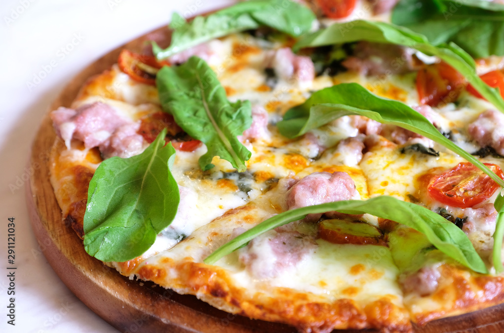 closeup italian sausage and reocket pizza on wood plate