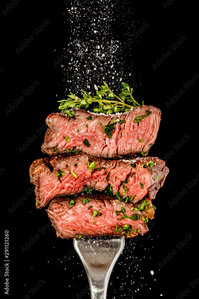 Sliced beef steak from grill on a fork. Salt is strewing from above - obrazy, fototapety, plakaty 
