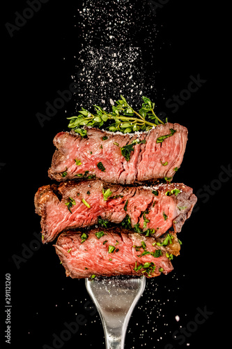 Sliced beef steak from grill on a fork. Salt is strewing from above