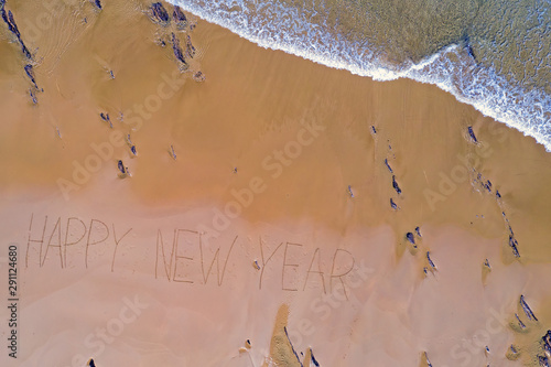 Aerial top shot from ocean waves and handwritten Happy New Year at the beach