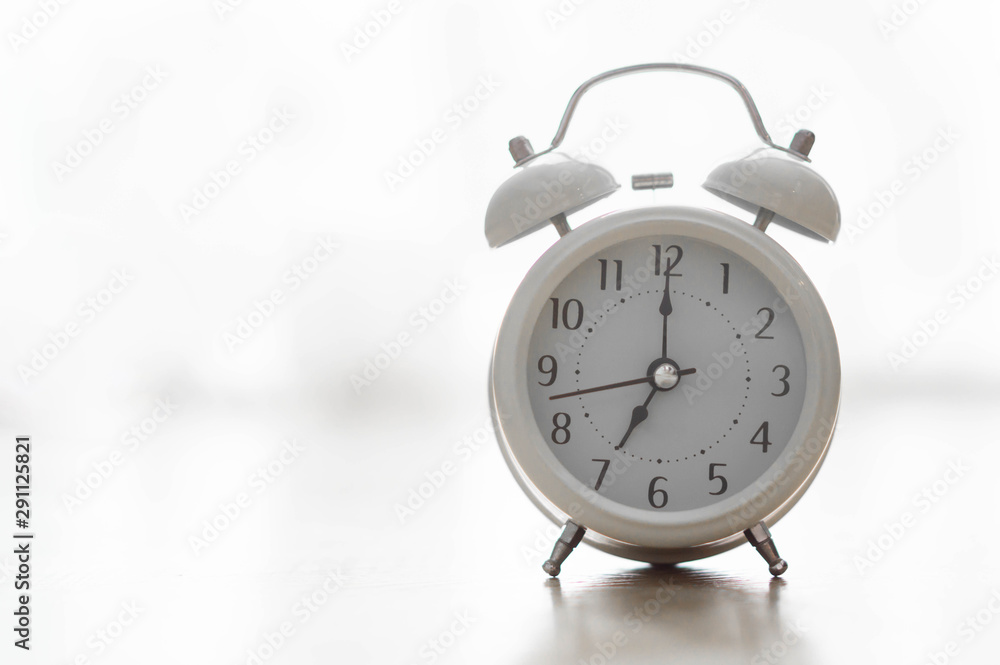Alarm clock on wooden table for wake up time with light from window, selective focus Alarm clock on wooden table for wake up time with light from window, selective focus