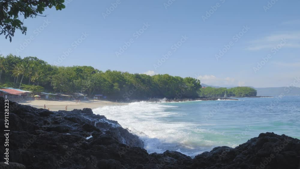 Tropical beach with big waves and white splashes on black rock with many people are swimming and walking in lagoon Tropical beach with big waves and white splashes on black rock with many people are swimming and walking in lagoon