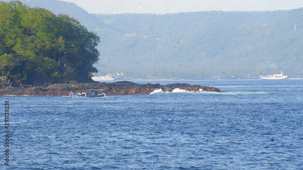 Small wooden traditinal balinese boat is passing rocky beach Small wooden traditinal balinese boat is passing rocky beach