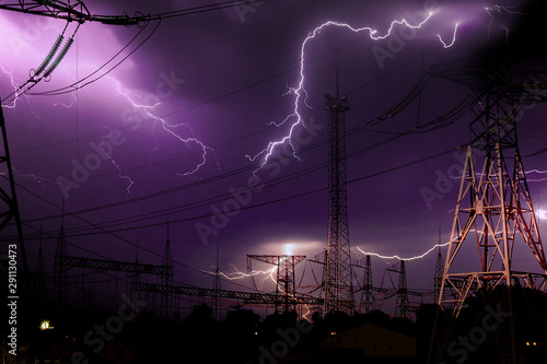 high voltage electrical substation illuminated by lightning flashes during an impending storm at night