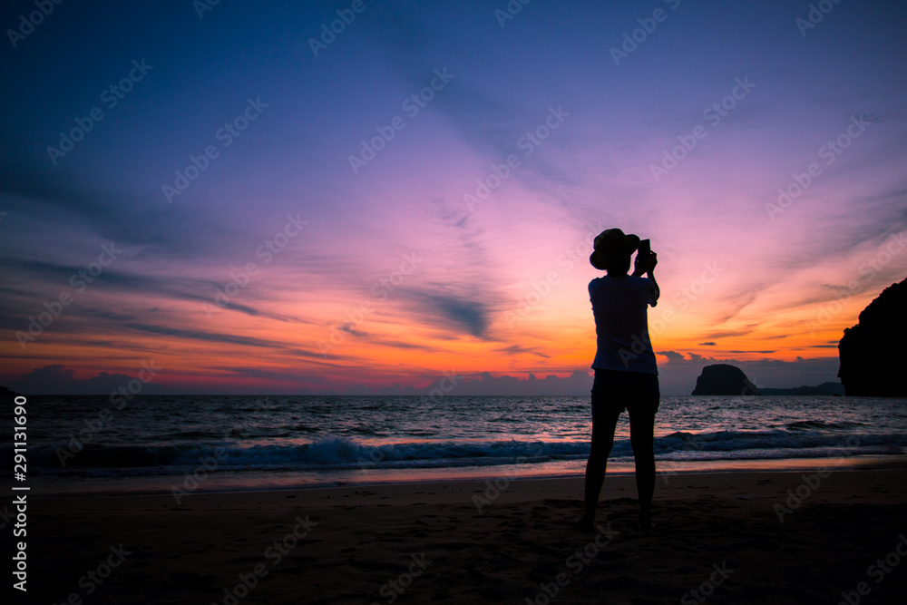 Fototapeta premium Silhouette of The girl is walking happily Use the phone at the beach during the sunset and her enjoying freedom feeling happy at sunset