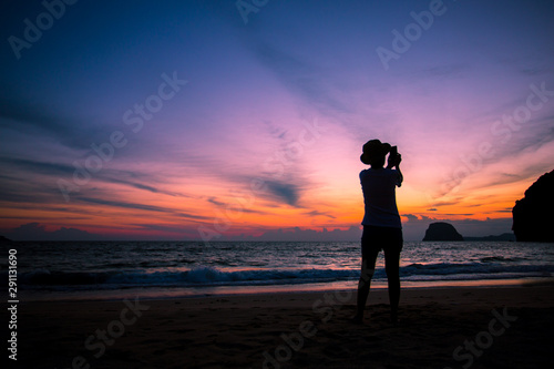 Silhouette of The girl is walking happily Use the phone at the beach during the sunset and her enjoying freedom feeling happy at sunset 