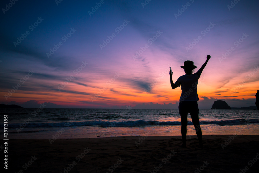 Silhouette of The girl is walking happily Use the phone at the beach during the sunset and her enjoying freedom feeling happy at sunset 
