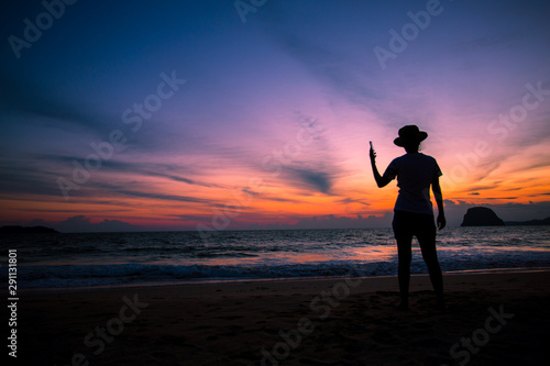 Silhouette of The girl is walking happily Use the phone at the beach during the sunset and her enjoying freedom feeling happy at sunset 