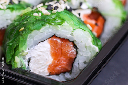Fresh prepared sushi rolls with chuka salad, seasame, red fish salmon and whit cheese filadelfia on plastic container. Close-up