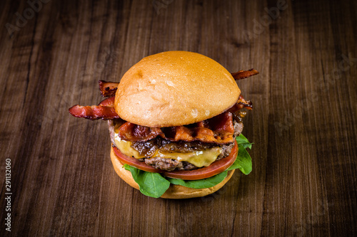 Craft beef burger with cheese, bacon, caramelized onion and rocket leafs on wood table and rustic background. photo