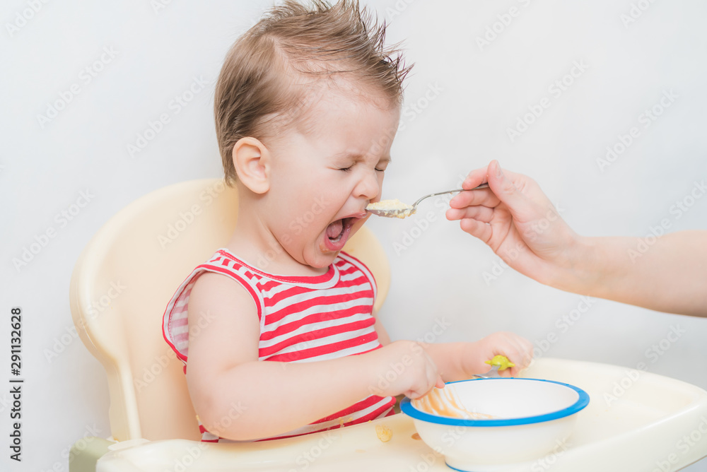 Mom feeds the baby buckwheat porridge in the kitchen Mom feeds the baby buckwheat porridge in the kitchen