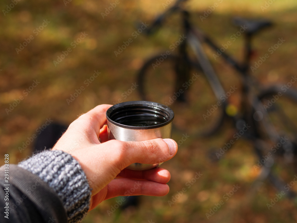 Hot Cup of tea in hand. Drink hot tea while riding a bike in the cold autumn weather Hot Cup of tea in hand. Drink hot tea while riding a bike in the cold autumn weather