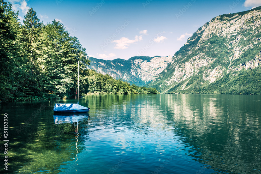 First sunlight glowing surface of Bohinj lake. Beautiful summer scene of Triglav national park. Great morning view of Julian Alps, Slovenia, Europe. Instagram filter toned.