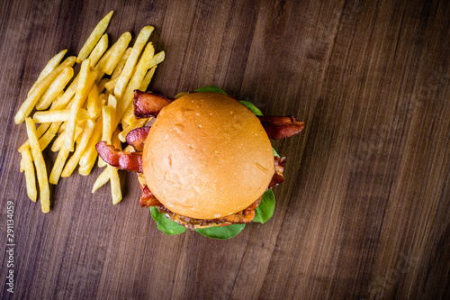 Craft beef burger with cheese, bacon, rocket leafs, caramelize onion and french fries on wood table and rustic background. photo