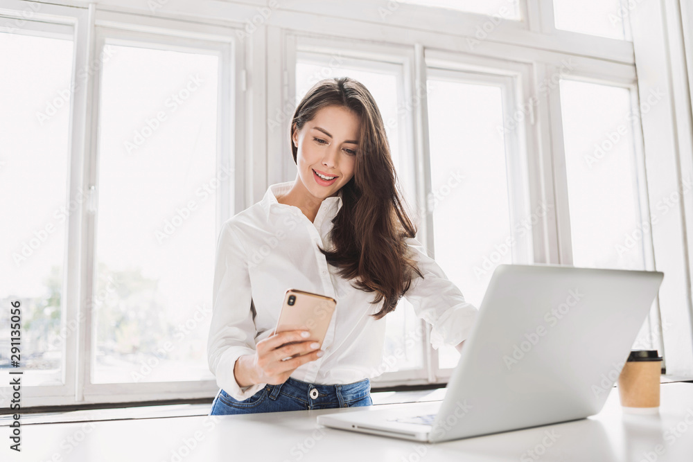 Woman using laptop and smartphone in office. Beautiful girl texting on phone at home. Entrepreneur, businesswoman, freelance worker, student working on computer. Business, technology concept Woman using laptop and smartphone in office. Beautiful girl texting on phone at home. Entrepreneur, businesswoman, freelance worker, student working on computer. Business, technology concept