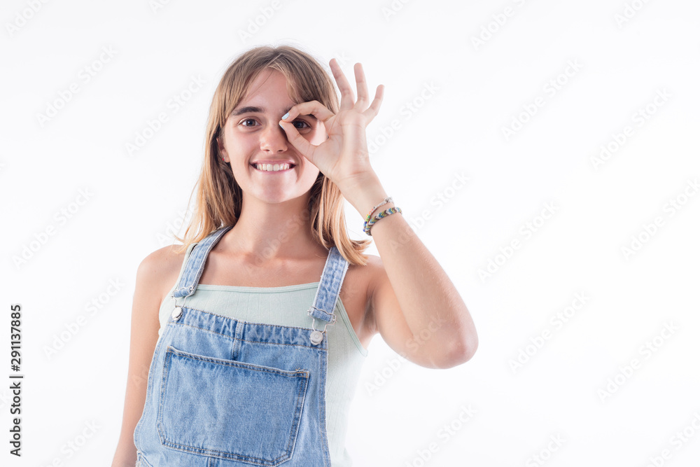 Funny amusing blonde girl in jeans dress showing okay gesture near her eye Funny amusing blonde girl in jeans dress showing okay gesture near her eye