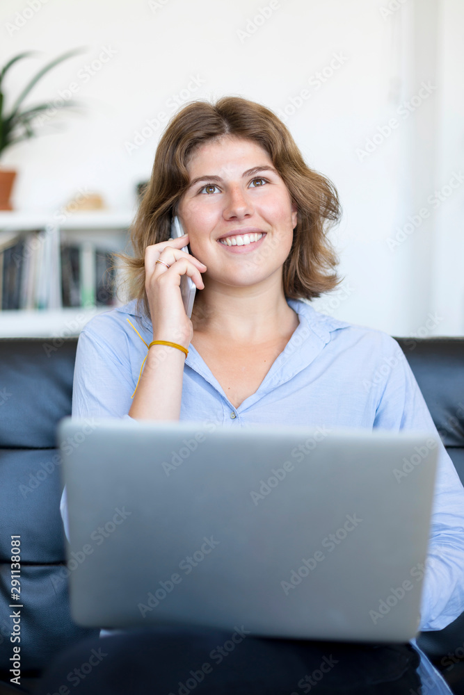 Entrepreneur woman wearing blue shirt working with a laptop sitting on a couch at home Entrepreneur woman wearing blue shirt working with a laptop sitting on a couch at home
