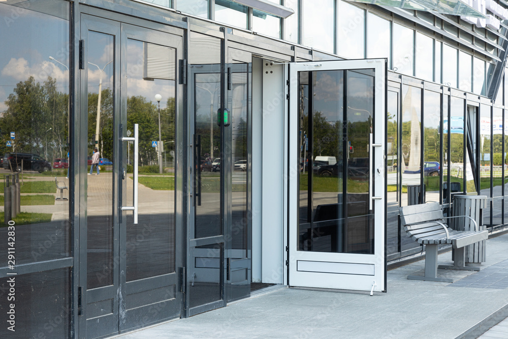 Entry to business or apartments building shiny facade with glass walls and doors with street reflection on it and a bench nearby