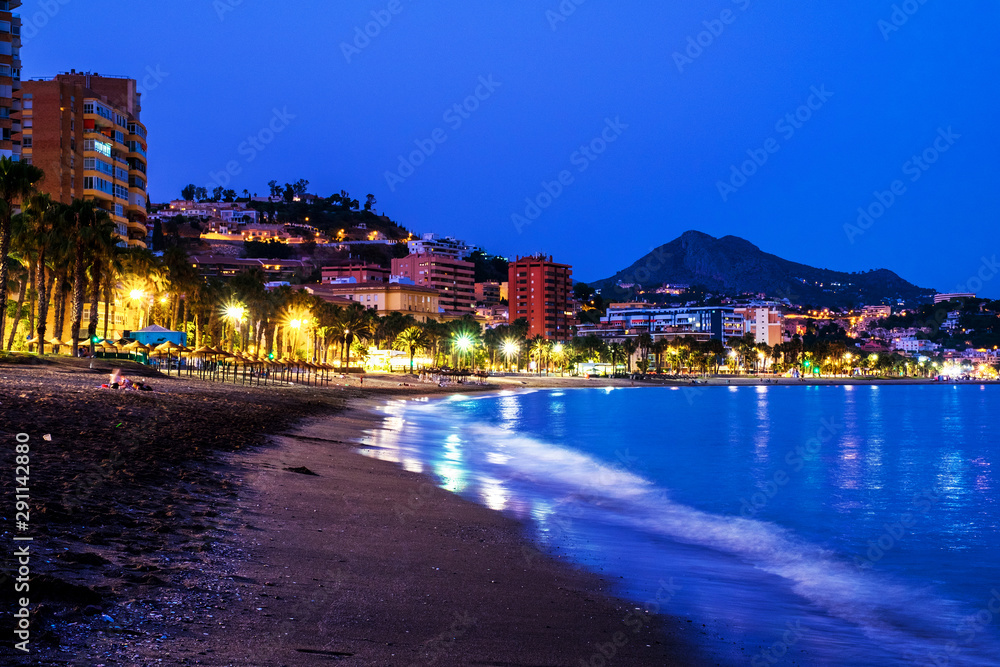 Fototapeta premium Famous Malagueta beach in Malaga, Spain at night. Coastline and motion blurred waves at sunset