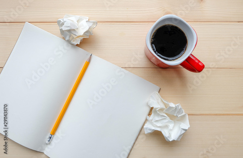 Top view: There are crumpled paper, blank pages of notebook, yellow pencil and hot coffee of red cup on wooden table. For brainstorming, work hard, stress concept