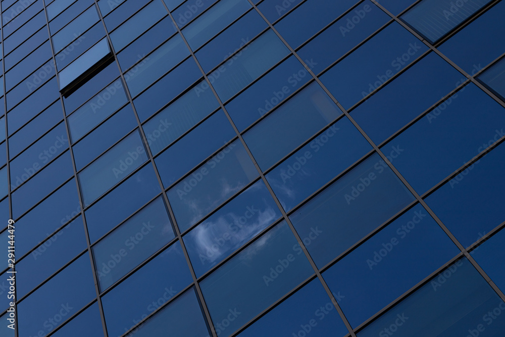 Ground view of blue glass surface of building wall reflecting blue sky with clouds Ground view of blue glass surface of building wall reflecting blue sky with clouds