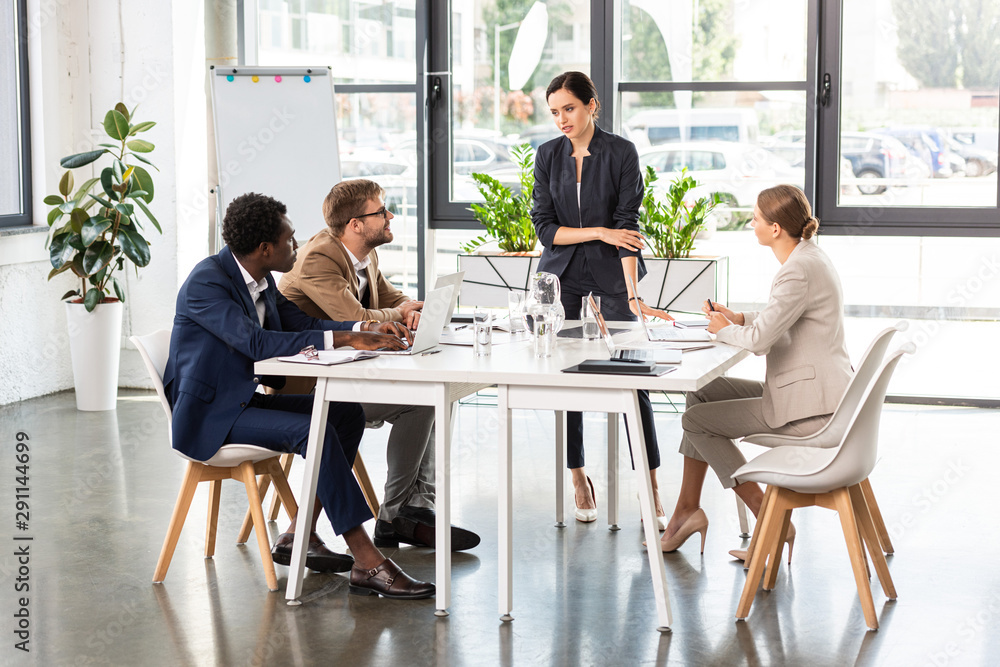 multiethnic businesspeople at tables with laptops during conference in office