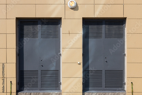 Beige tiled wall with two grey metal doors and a light in the middle above them photo