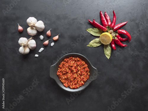 Red hot sauce, garlic, red pepper and spices on a black table. Top view. 