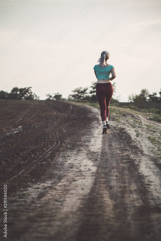 back of young woman in sportswear running distance in the field, girl engaged in sport outdoors, concept healthy lifestyle and bodycare