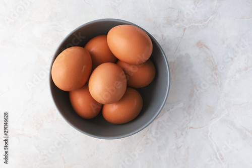 Fresh chicken eggs in gray bowl on white marble table background. Farm products, natural organic eggs