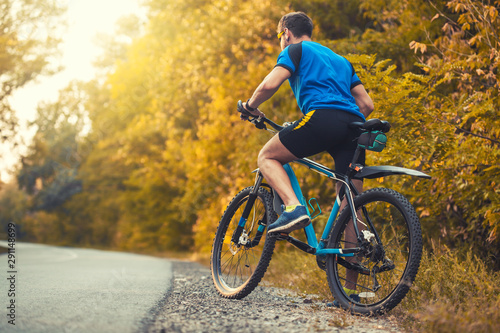 man cyclist rides in the sunny forest on a mountain bike. Adventure travel. back view