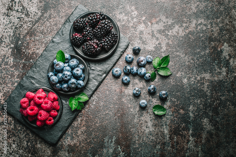 Fresh berries with raspberries, blueberries, blackberries in bowl on a stone stand on a dark metal background. - obrazy, fototapety, plakaty 