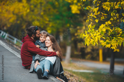 Beautiful happy young family with one child sitting together on trail in autumn season