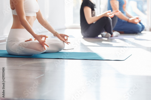 Unidentified young woman yoga instructor sitting in lotus position and meditating on a mat in the gym. concept of meditation and stretching. Copyspace