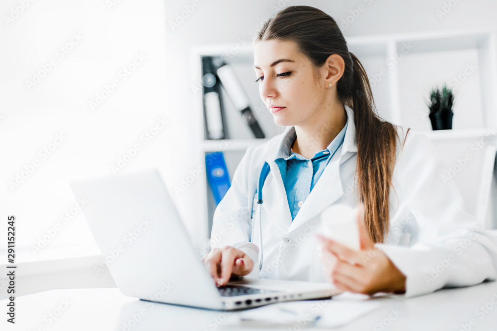 Smiling young female doctor working at the clinic , she is using a computer and writing medical reports. Smiling young female doctor working at the clinic , she is using a computer and writing medical reports.