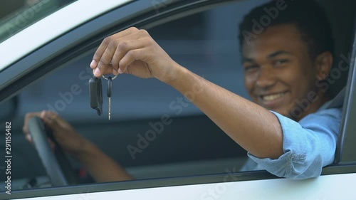 Happy black male teenager on driver place showing car keys, first automobile