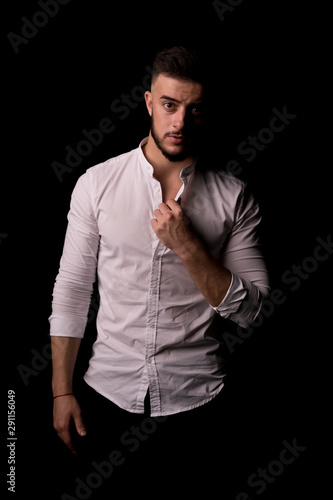 Thoughtful young brunette man in white shirt thinking about something isolated on a black background. Vertical photo. © Ivan