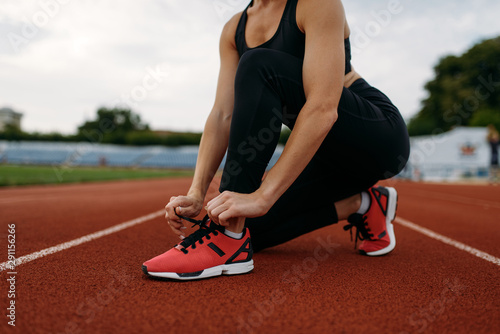 Female runner tying her shoelaces on stadium