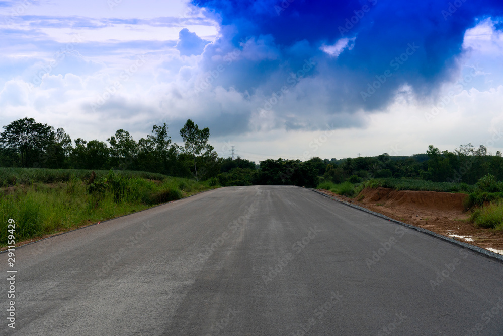 An empty asphalt road is a direct way. With nature of plantation and forest under blue sky. Road around of Ang Kep Nam Dok Krai Rayong Thailand,