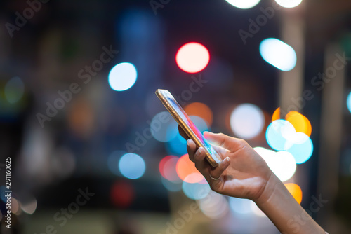 The woman's hand is using a smartphone on the road and has beautiful bokeh lights.