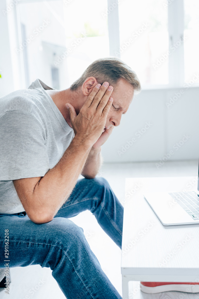 Fototapeta premium side view of handsome man in t-shirt with closed eyes touching head in apartment