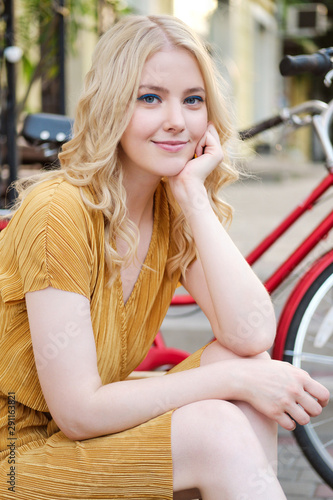 Portrait of beautiful romantic blond girl in dress dreamily looking in camera on street