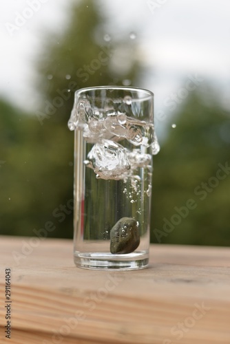 A transparent glass with water, a stone with the inscription "Rybinsk Volga", splashes and air bubbles on a wooden stand.